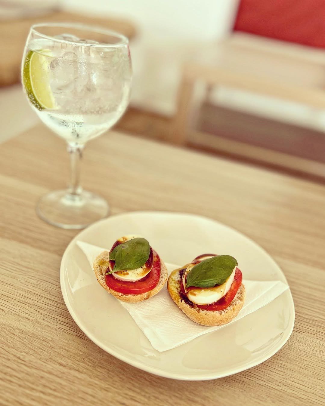 Duas bruschettas com tomate, queijo branco e manjericão num prato, ao lado de um copo com limão