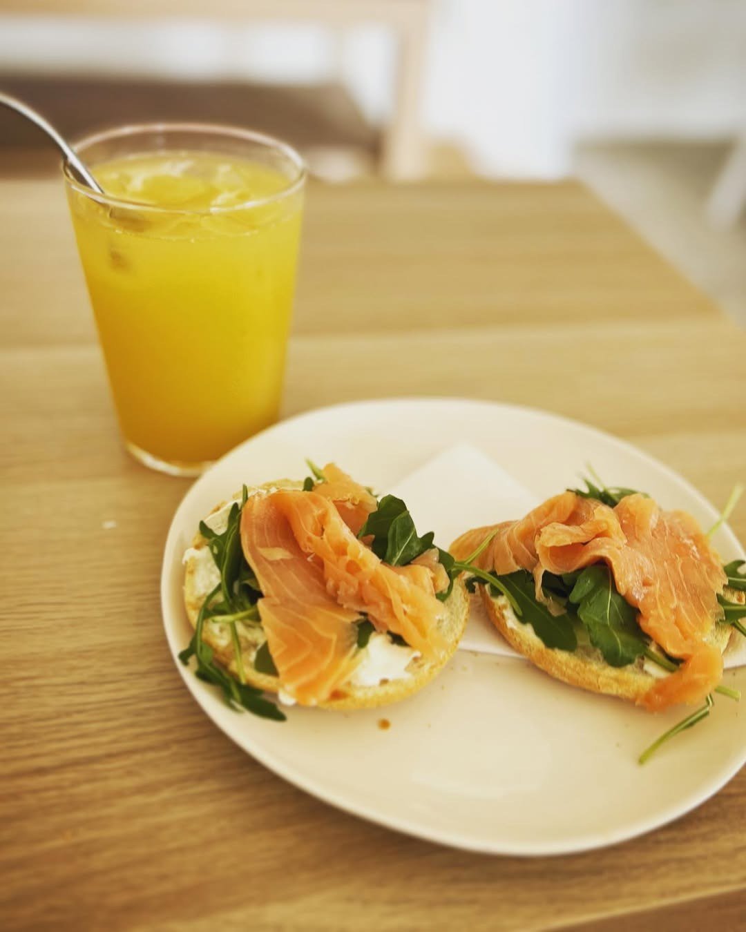 Duas bruschettas com salmão fumado e rúcula num prato, com um sumo de laranja ao lado