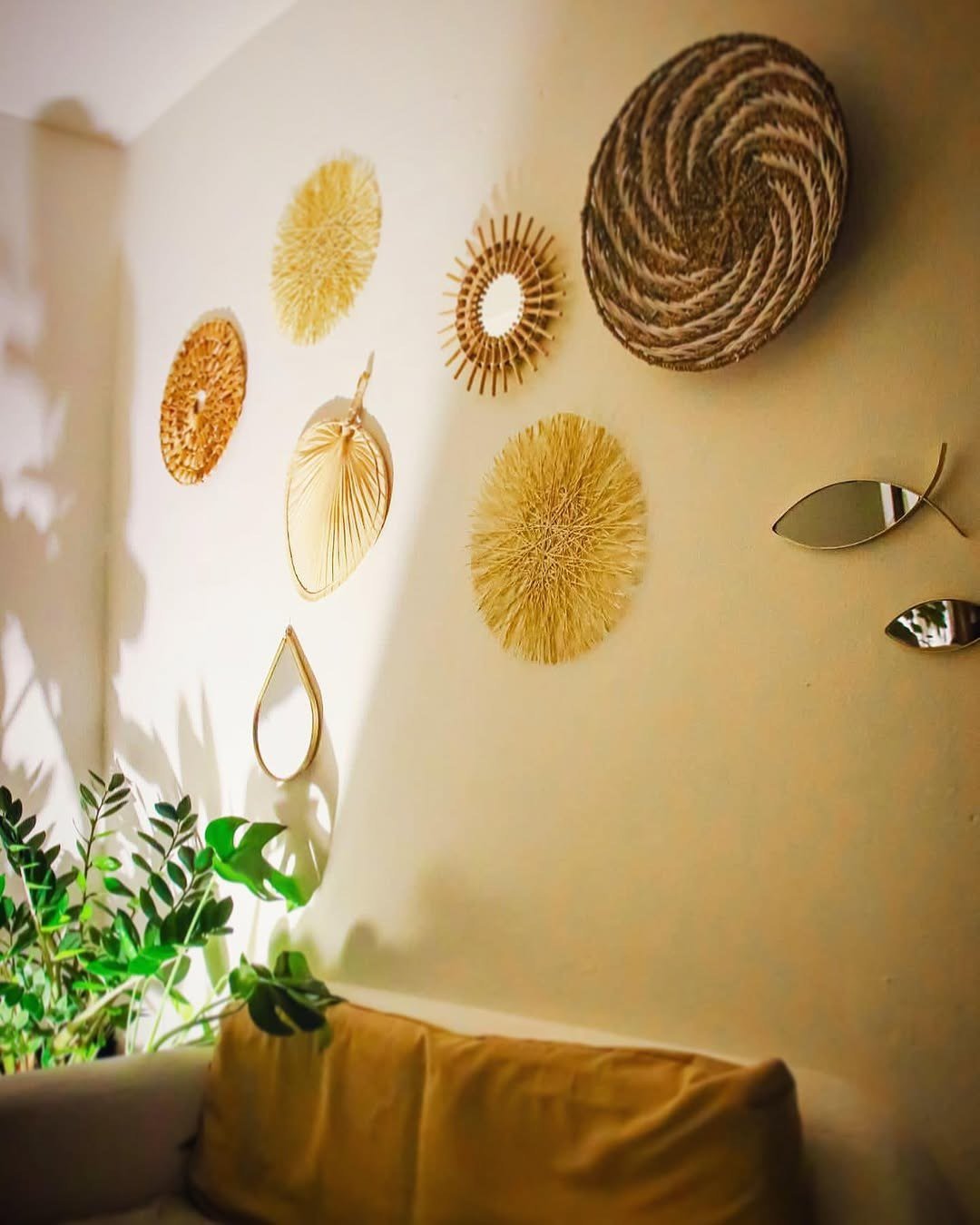Recanto interior com sofá mostarda, plantas e pratos de palha decorativos na parede